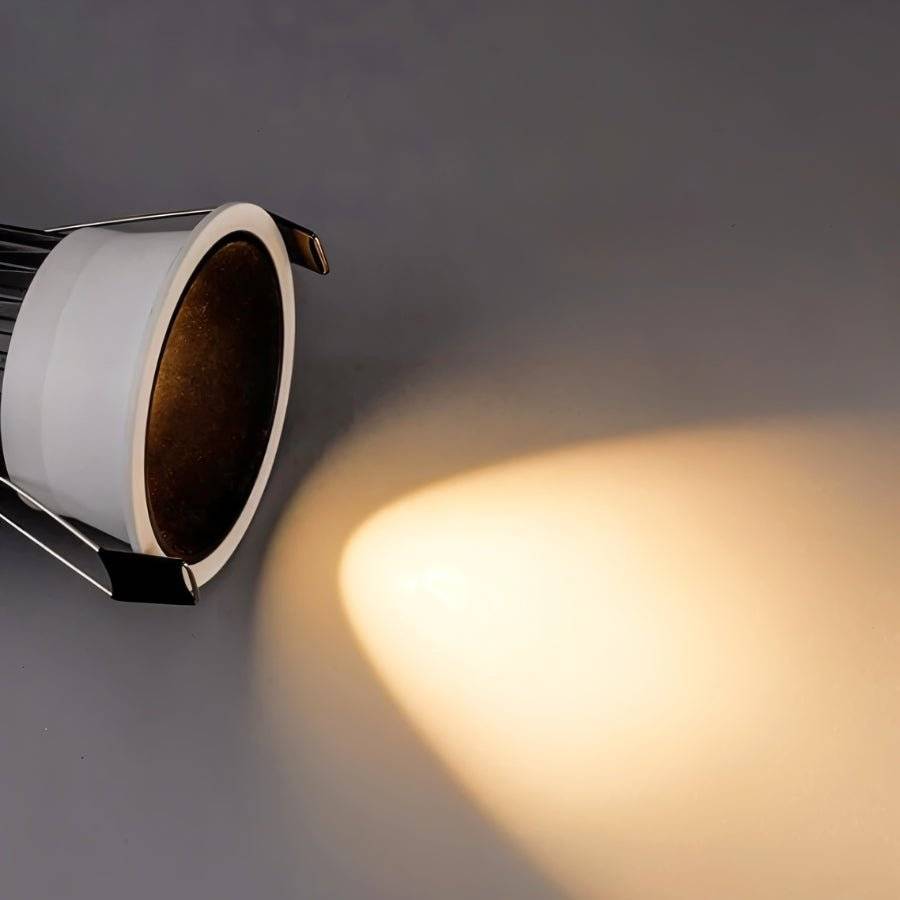Close angled view of the Clérachic recessed downlight, its baffle casting a warm white beam across a grey wall.