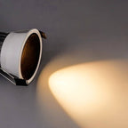 Close angled view of the Clérachic recessed downlight, its baffle casting a warm white beam across a grey wall.