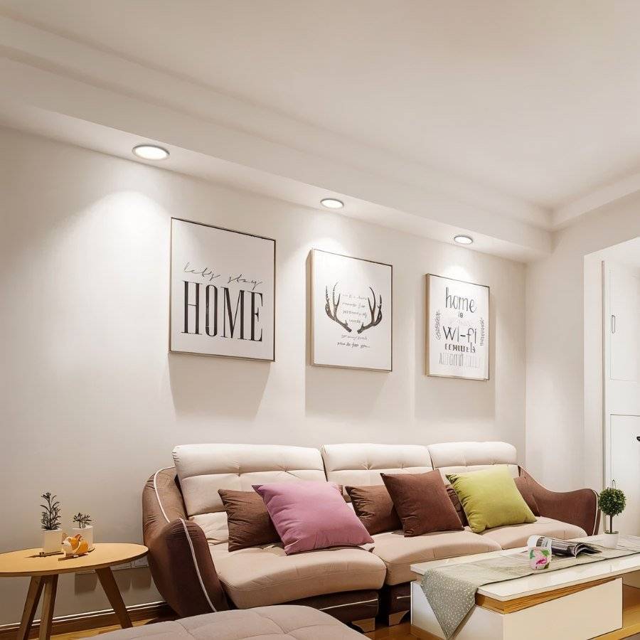 Three Clérachic white recessed downlights glowing warm white above a row of framed prints and a beige sofa.