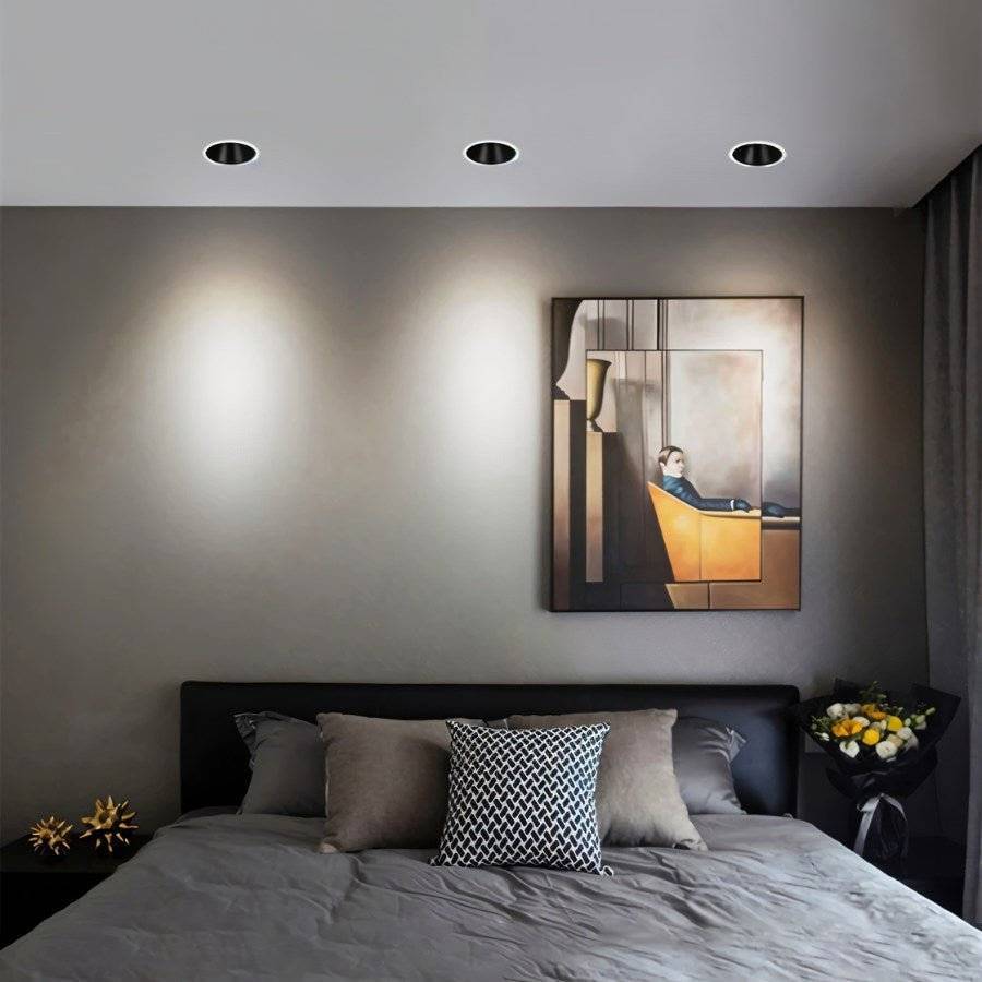 Three Clérachic black recessed downlights glowing cool white above a bed and a framed painting in a grey bedroom.