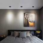 Three Clérachic black recessed downlights glowing cool white above a bed and a framed painting in a grey bedroom.
