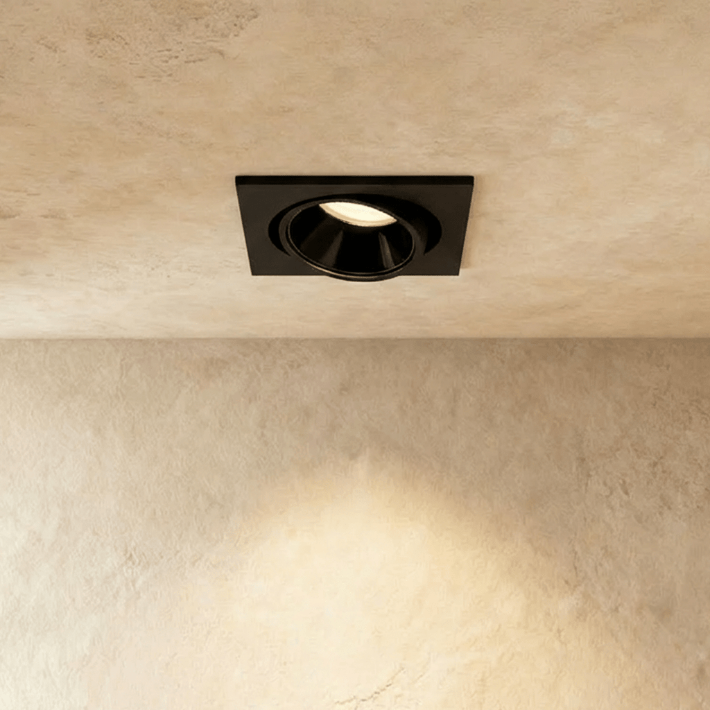 Clérachic recessed downlight in black, its square plate and tiltable head glowing warm white against a plastered ceiling.