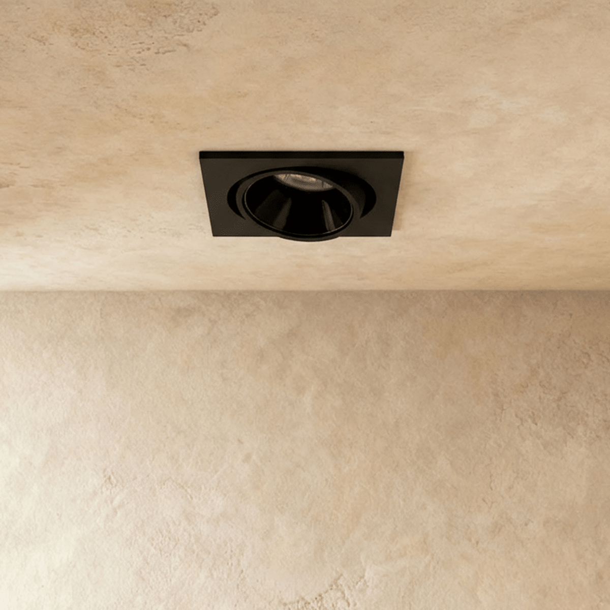 Straight-on view of the Clérachic black recessed downlight, its round tiltable head glowing warm white overhead.