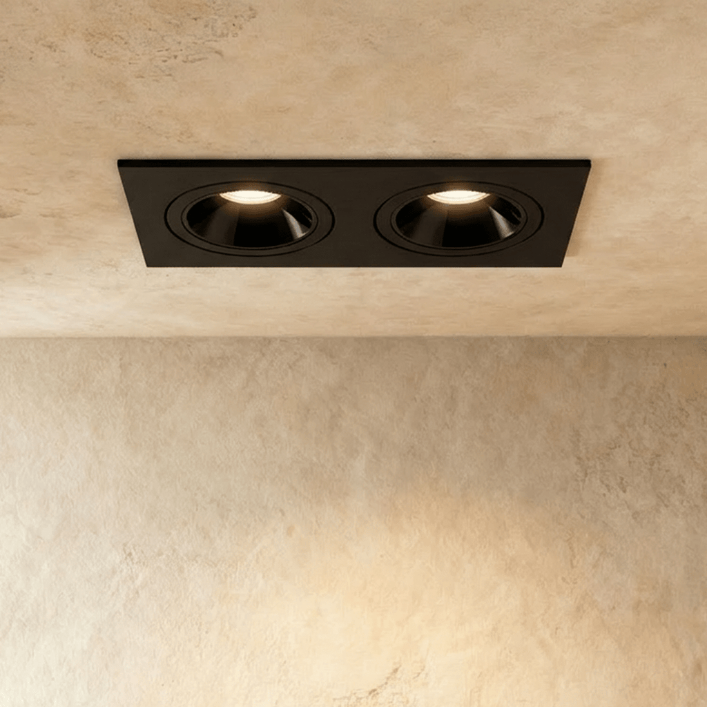 The Clérachic two-head recessed downlight in black, both tiltable heads glowing warm white against a plaster ceiling.