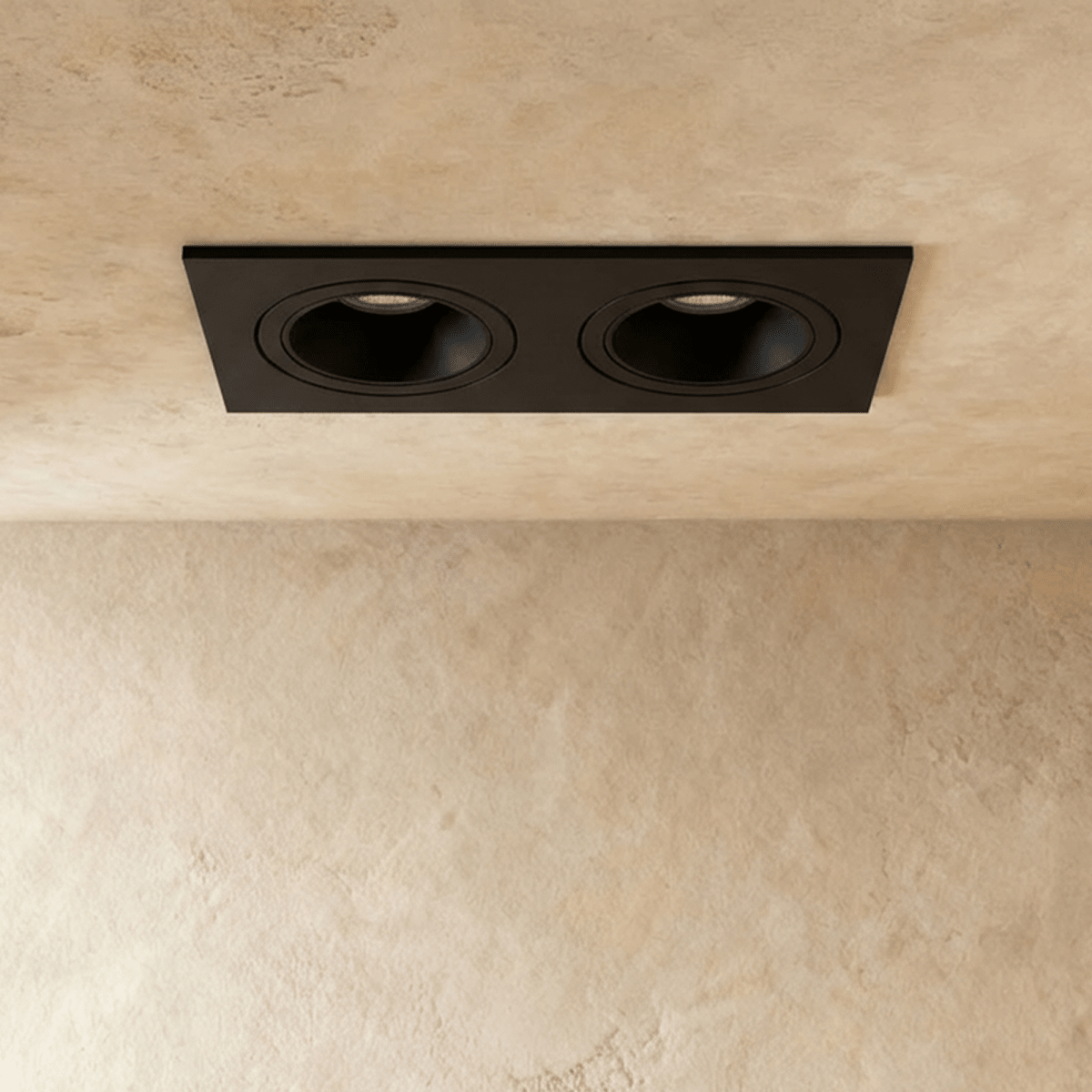 Straight-on view of the Clérachic black two-head recessed downlight, its tiltable heads glowing warm white overhead.