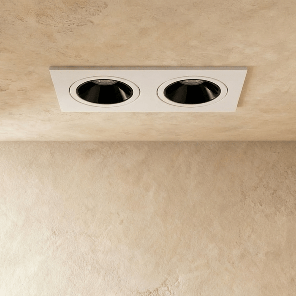 Close angle of the Clérachic white two-head recessed downlight, its tiltable heads glowing warm white overhead.