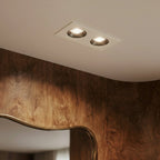 Close angle of the Clérachic white two-head recessed downlight glowing warm white beside a wood-panelled wall.