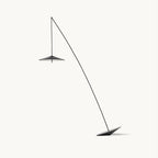 Black floor lamp with a long angled stem and a flat disc shade hanging from its tip, on a plain white backdrop, from Clérachic.