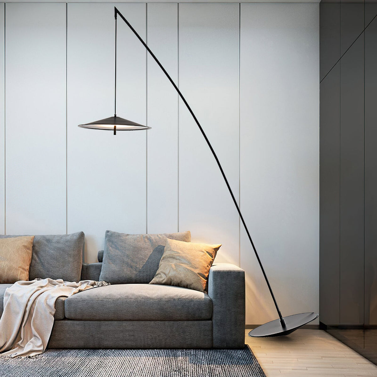 Angled black stem arcs over a grey sofa with soft cushions, a flat disc shade hanging beside a pale panelled wall, a Clérachic floor lamp.