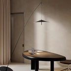 Black floor lamp leans over a dark oval wooden desk in a warm beige room with long curtains, its disc shade hanging mid-air, from Clérachic.
