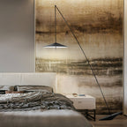 A black arc floor lamp hangs its disc shade in front of a painted landscape-style wall panel above a bed, from Clérachic.