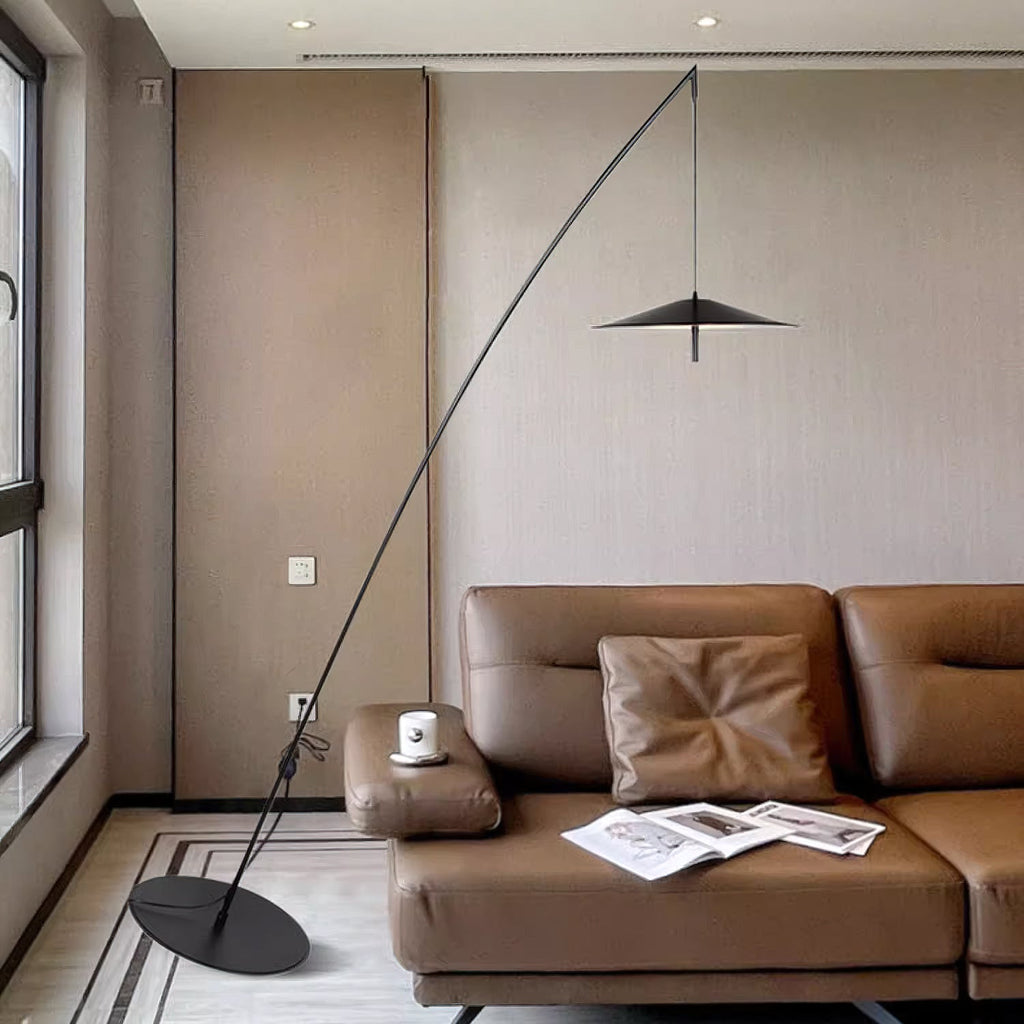 Black floor lamp with a round base beside a tan leather sofa, the disc shade hanging high in a room with tall windows, from Clérachic.