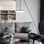 Lit disc shade hangs above a grey sofa with teal cushions, in a room with shelves, plants and a dark green chair, from Clérachic.