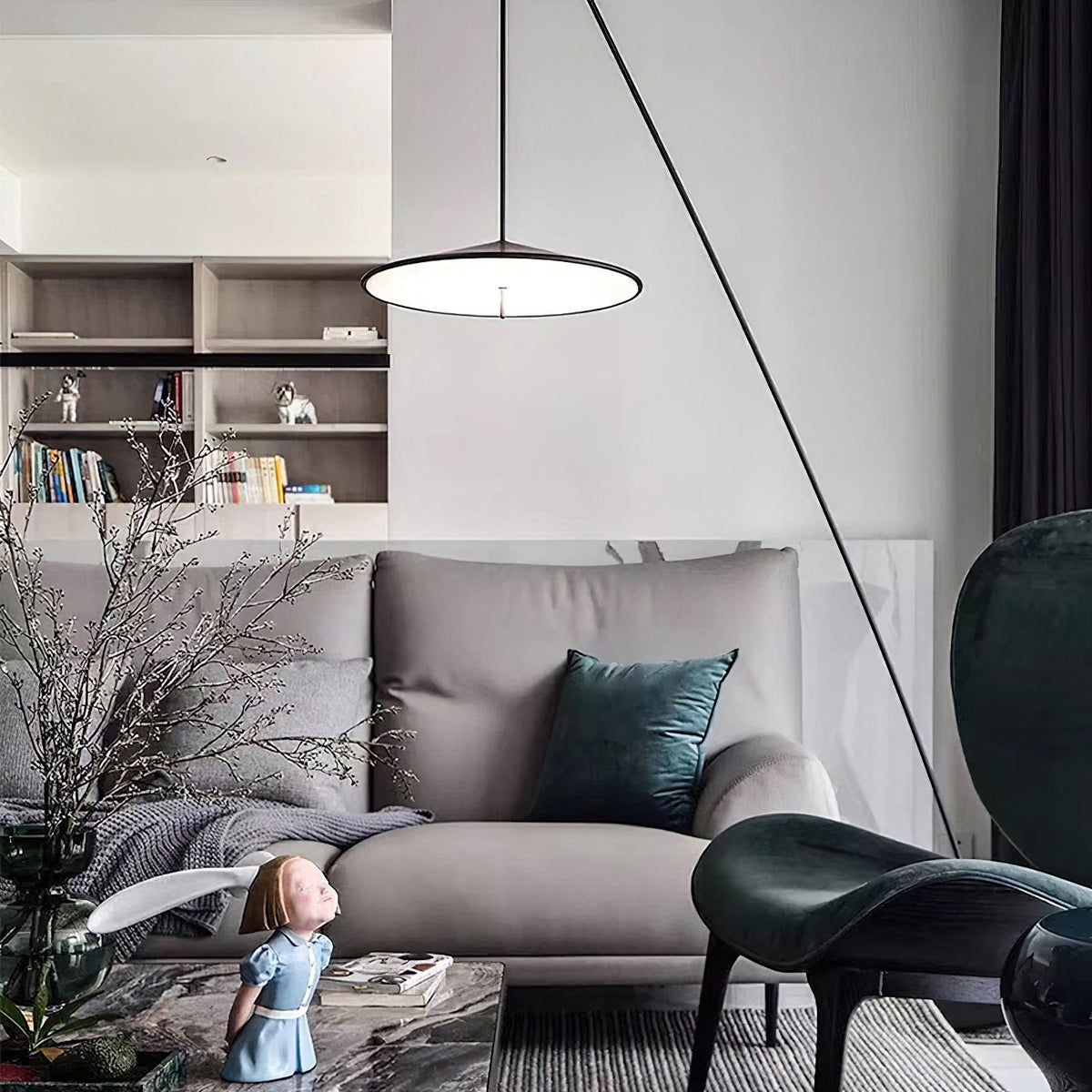 Lit disc shade hangs above a grey sofa with teal cushions, in a room with shelves, plants and a dark green chair, from Clérachic.