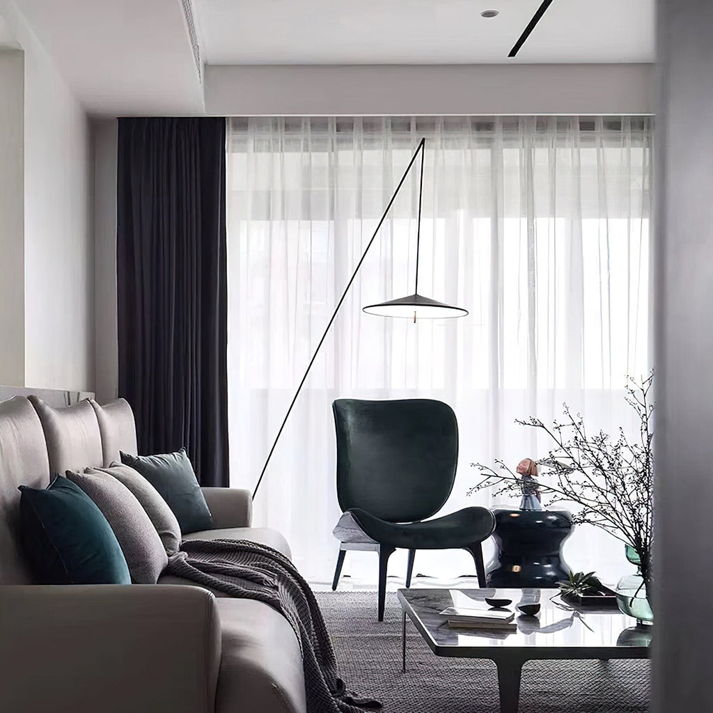 Fine black stem rises across sheer curtains over a grey sofa and dark green armchair, the disc shade hanging in the room, a Clérachic floor lamp.