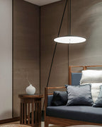 Lit disc shade hangs low beside a wooden-framed sofa and a round side table with a white vase, a Clérachic floor lamp.
