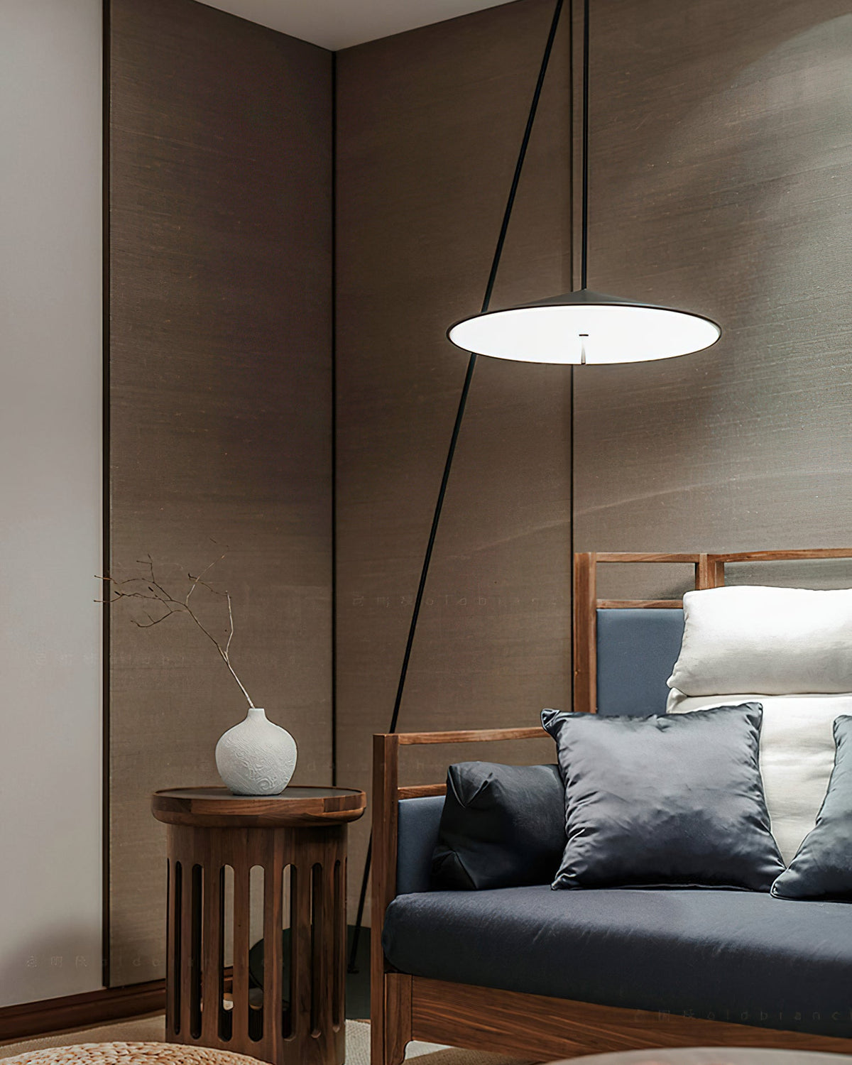 Lit disc shade hangs low beside a wooden-framed sofa and a round side table with a white vase, a Clérachic floor lamp.
