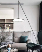 Disc shade lit from below in a bright living room with shelves, a grey sofa and a teal cushion, from Clérachic.