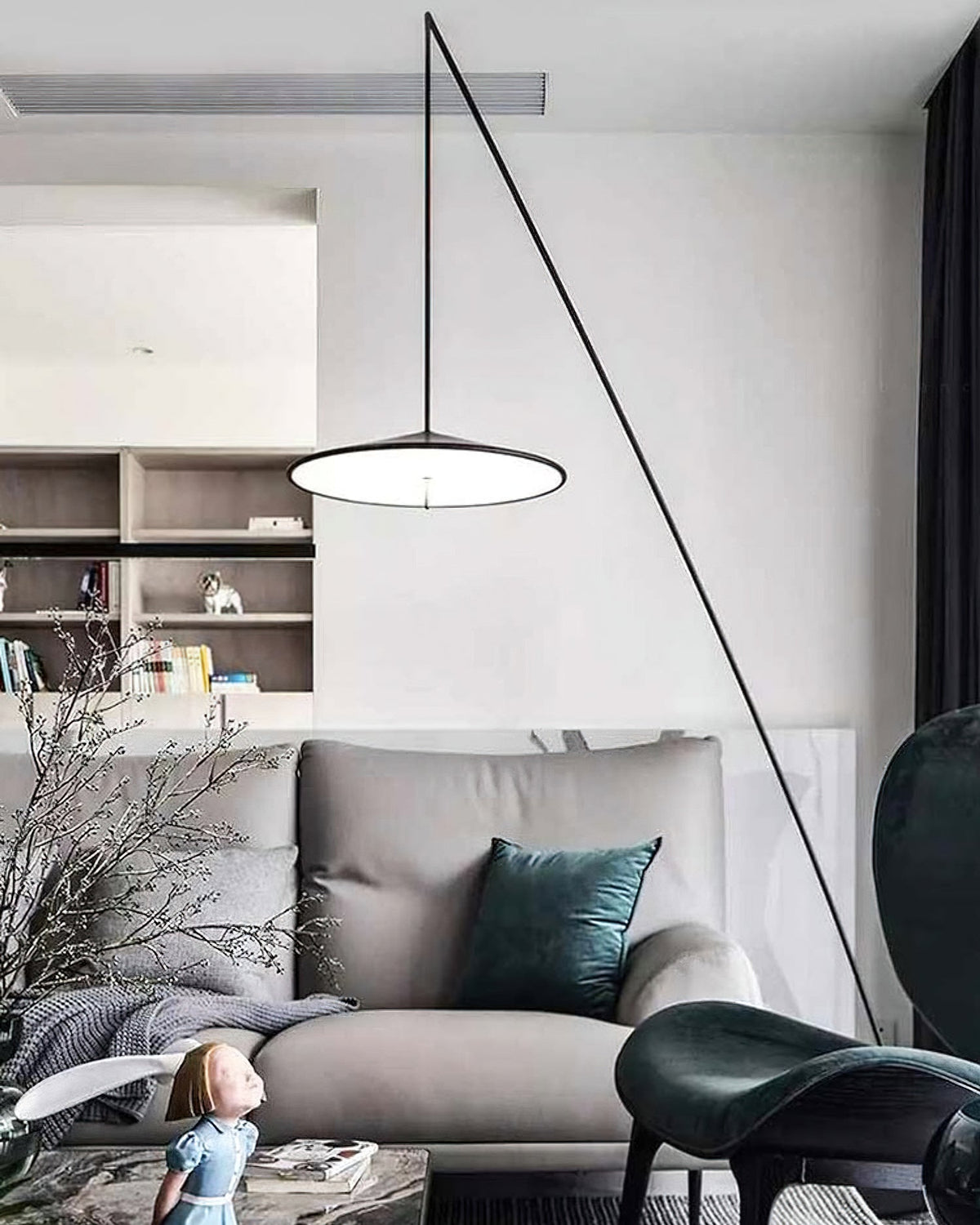 Disc shade lit from below in a bright living room with shelves, a grey sofa and a teal cushion, from Clérachic.