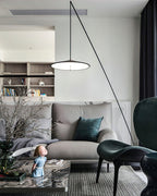 Vertical view of a lit disc shade above a grey sofa with a teal cushion and a figurine on the table, a Clérachic floor lamp.