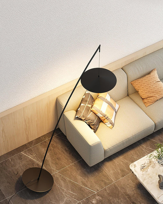 Seen from above, the black disc shade hangs near a cream sofa with orange cushions on a tiled floor, from Clérachic.