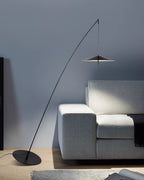 Black arc floor lamp against a blue-grey wall, with a pale grey sofa and a tilted round base on the floor, from Clérachic.