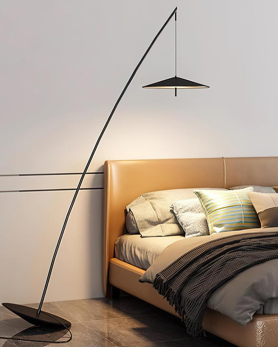 Black stem curves over a bed with a tan leather headboard and striped cushions, the disc shade lit above, a Clérachic floor lamp.