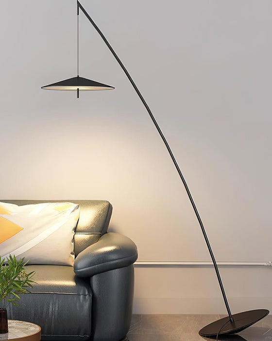 Disc shade lit warm above a dark leather armchair with a green plant, the stem arcing across a grey wall, from Clérachic.