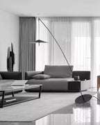Wide monochrome living room with a low sofa and marble coffee table, a Clérachic floor lamp arcing in from the right.