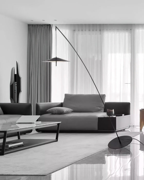 Wide monochrome living room with a low sofa and marble coffee table, a Clérachic floor lamp arcing in from the right.