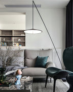 Disc shade glowing above a grey sofa, with shelves behind and a teal cushion on the seat, a Clérachic floor lamp.