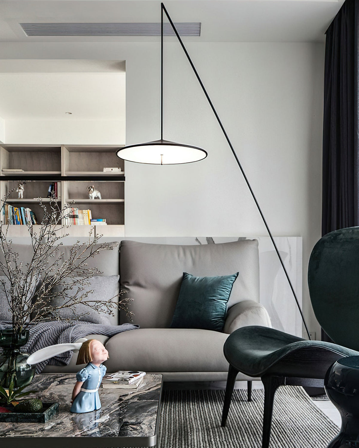 Disc shade glowing above a grey sofa, with shelves behind and a teal cushion on the seat, a Clérachic floor lamp.