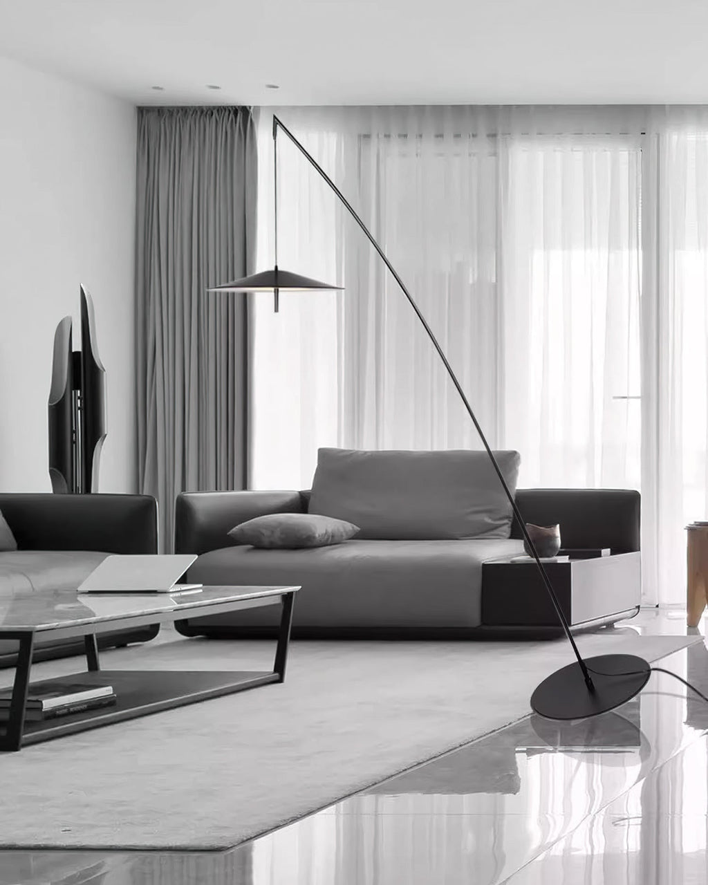 Greyscale room with sheer curtains, a dark sofa and a coffee table, and a slim black floor lamp leaning over them from Clérachic.