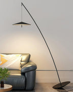 Warm-lit wall above a green-grey leather sofa, with the black arc stem and disc shade overhead, a Clérachic floor lamp.