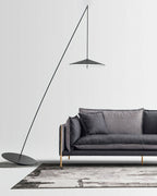 Black stem and disc shade stand over a charcoal sofa on a grey rug against a white wall, from Clérachic.