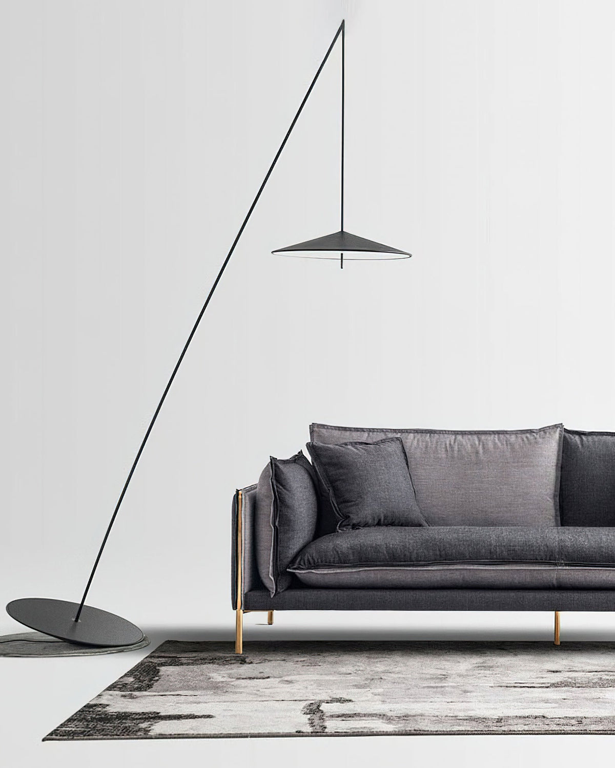 Black stem and disc shade stand over a charcoal sofa on a grey rug against a white wall, from Clérachic.