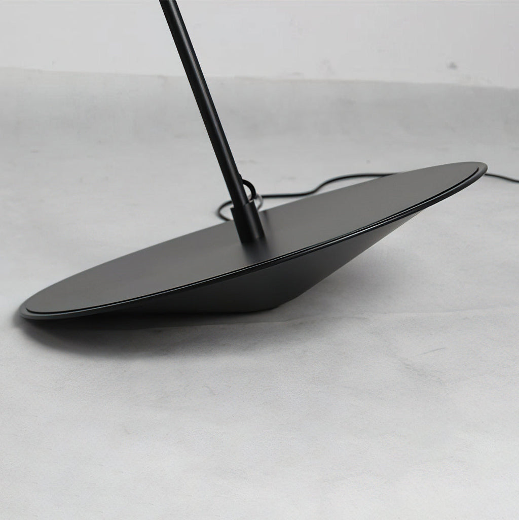 Close view of the round black base, tilted on a concrete-grey floor, with the stem and cord leaving it, on this Clérachic floor lamp.