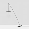 Full view of the black stem, disc shade and tilted base against a pale grey wall and floor, a Clérachic floor lamp.