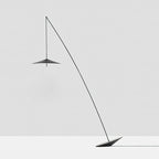 Full view of the black stem, disc shade and tilted base against a pale grey wall and floor, a Clérachic floor lamp.