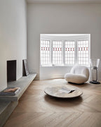 Distant Clérachic floor lamp in the corner of a living room with a bay window, a round low table and a cream boucle chair.
