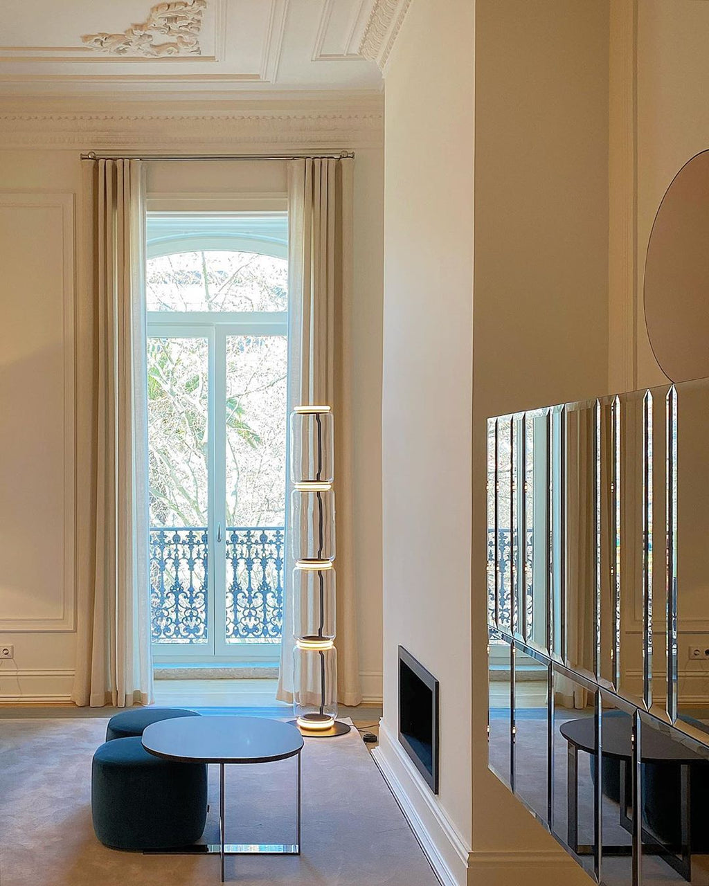 Distant Clérachic floor lamp by a tall window with a balcony, in a high-ceilinged room with a round table and a mirrored wall.