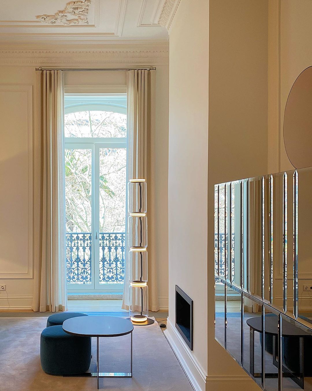Distant Clérachic floor lamp by a tall window with a balcony, in a high-ceilinged room with a round table and a mirrored wall.