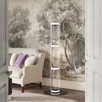 Clérachic floor lamp with a glass bowl on top, lit beside an armchair with a lilac cushion, in front of a tree mural.