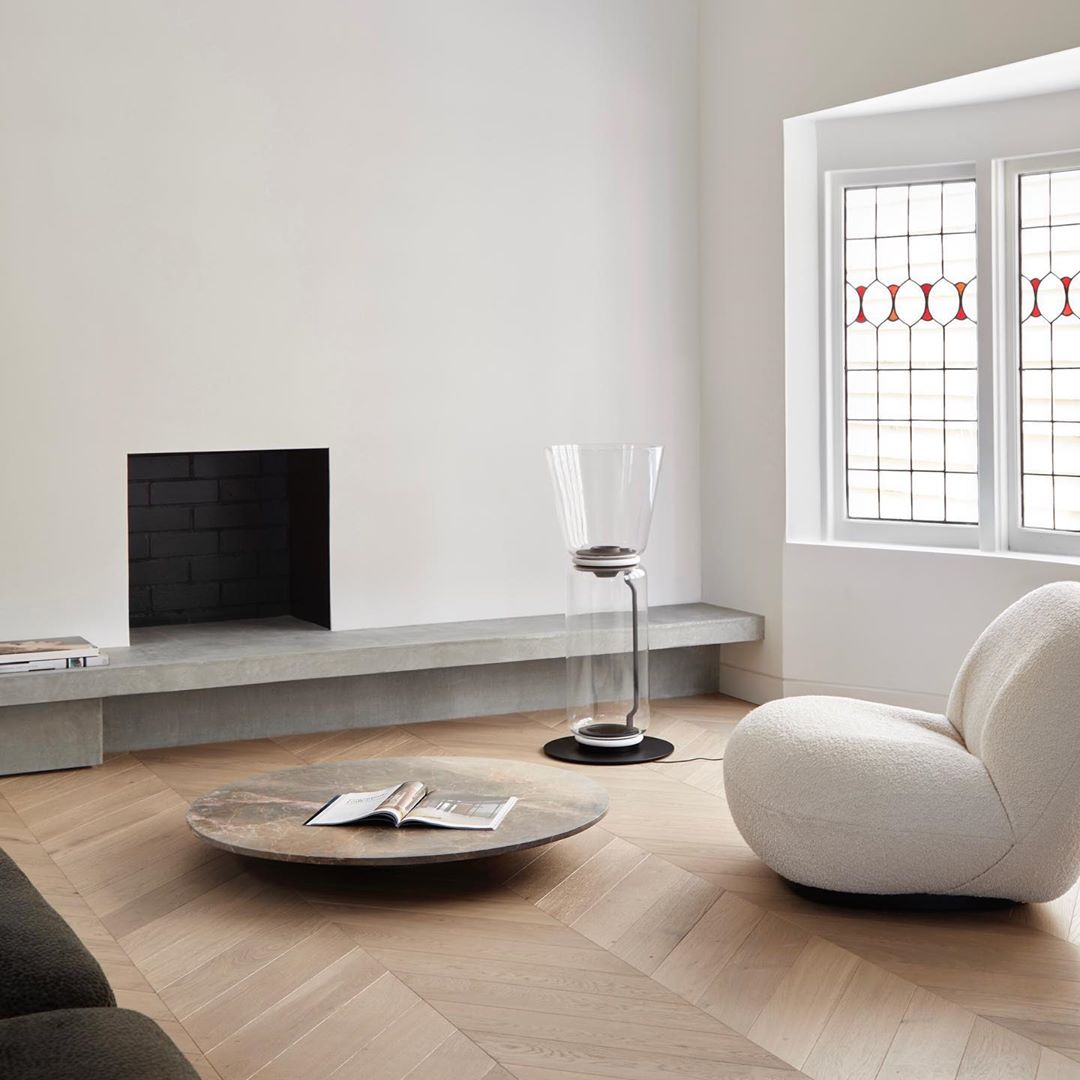 Clérachic floor lamp seen from across a pale living room, beside a grey fireplace, a round low table and a cream boucle chair.