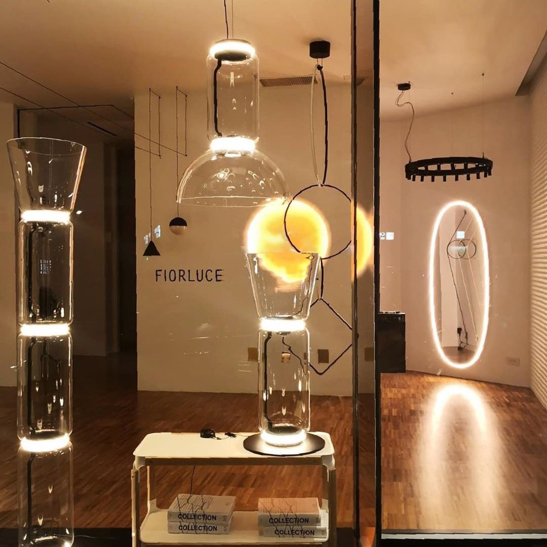 Showroom view with a Clérachic floor lamp at the left and a flared one at the centre, near other lights and an oval lit mirror.