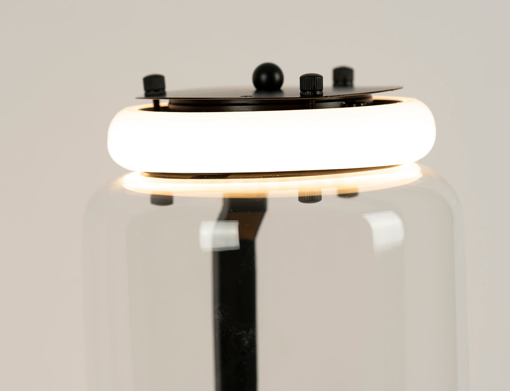 Close view of a glowing ring light at a join on this Clérachic floor lamp, with the black cap plate and screws above the glass.