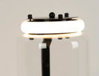 Close view of a glowing ring light at a join on this Clérachic floor lamp, with the black cap plate and screws above the glass.