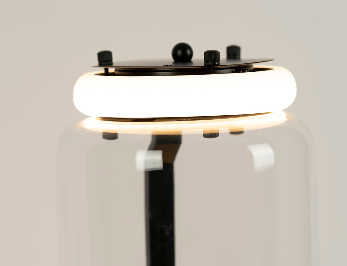Close view of a glowing ring light at a join on this Clérachic floor lamp, with the black cap plate and screws above the glass.