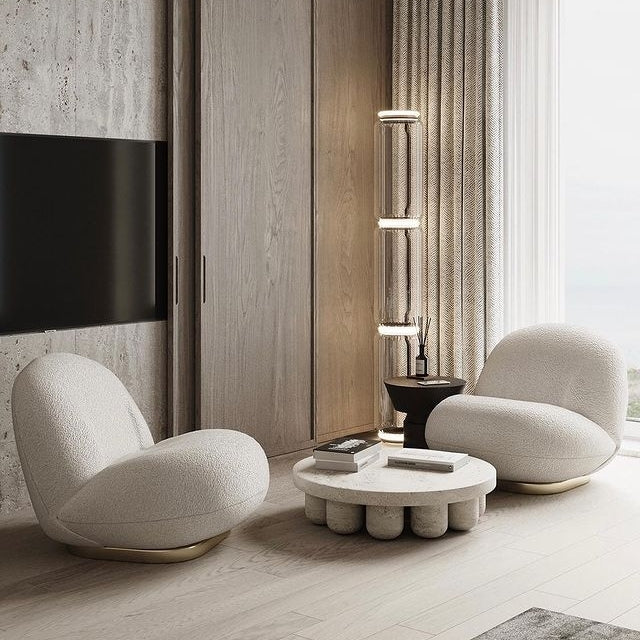 A Clérachic floor lamp of stacked glass cylinders seen small in a cream living room with boucle chairs and a round coffee table.