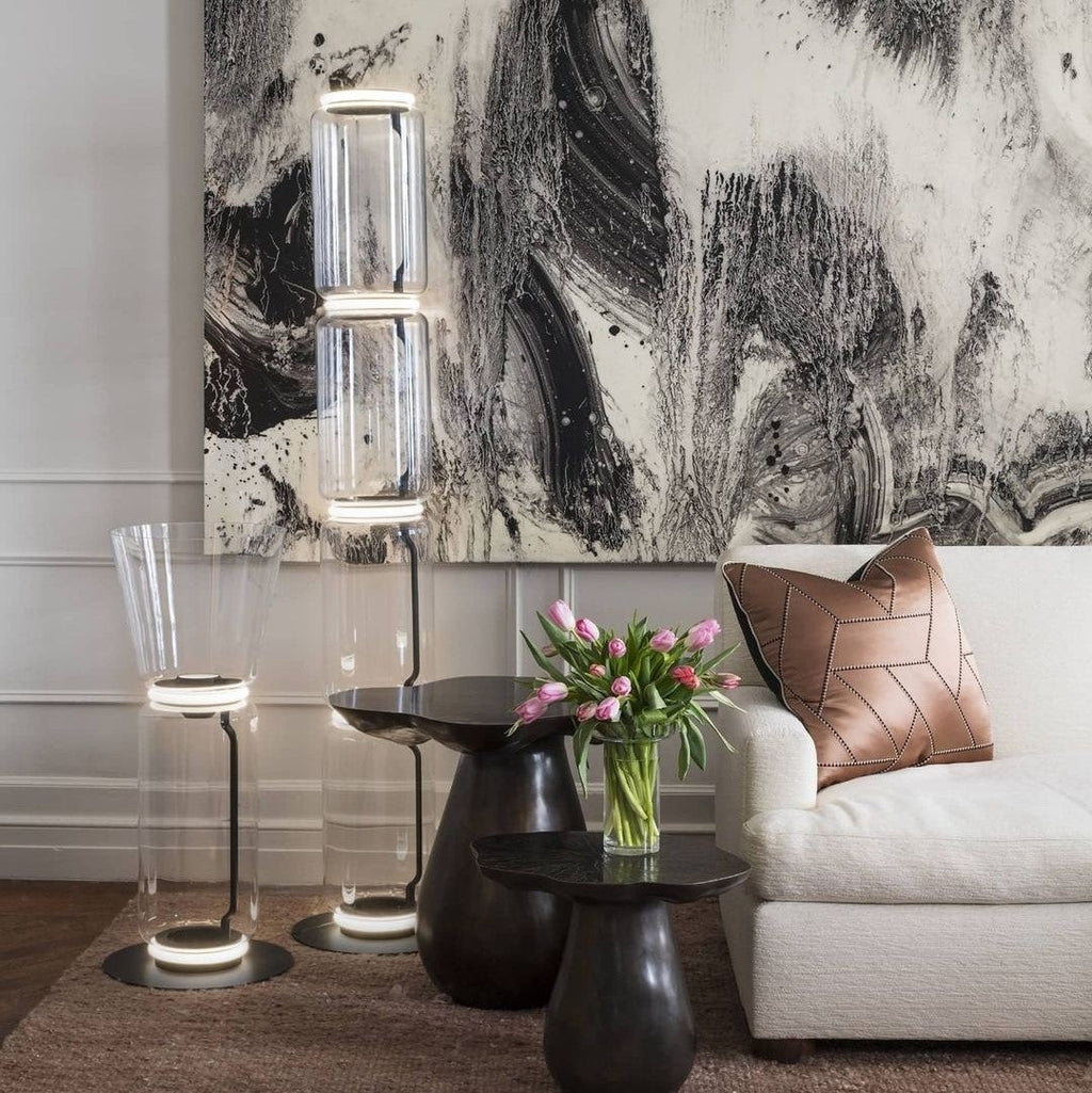 Two Clérachic floor lamps in a living room, one with a flared glass top, set before a large black and white painting and a cream sofa.